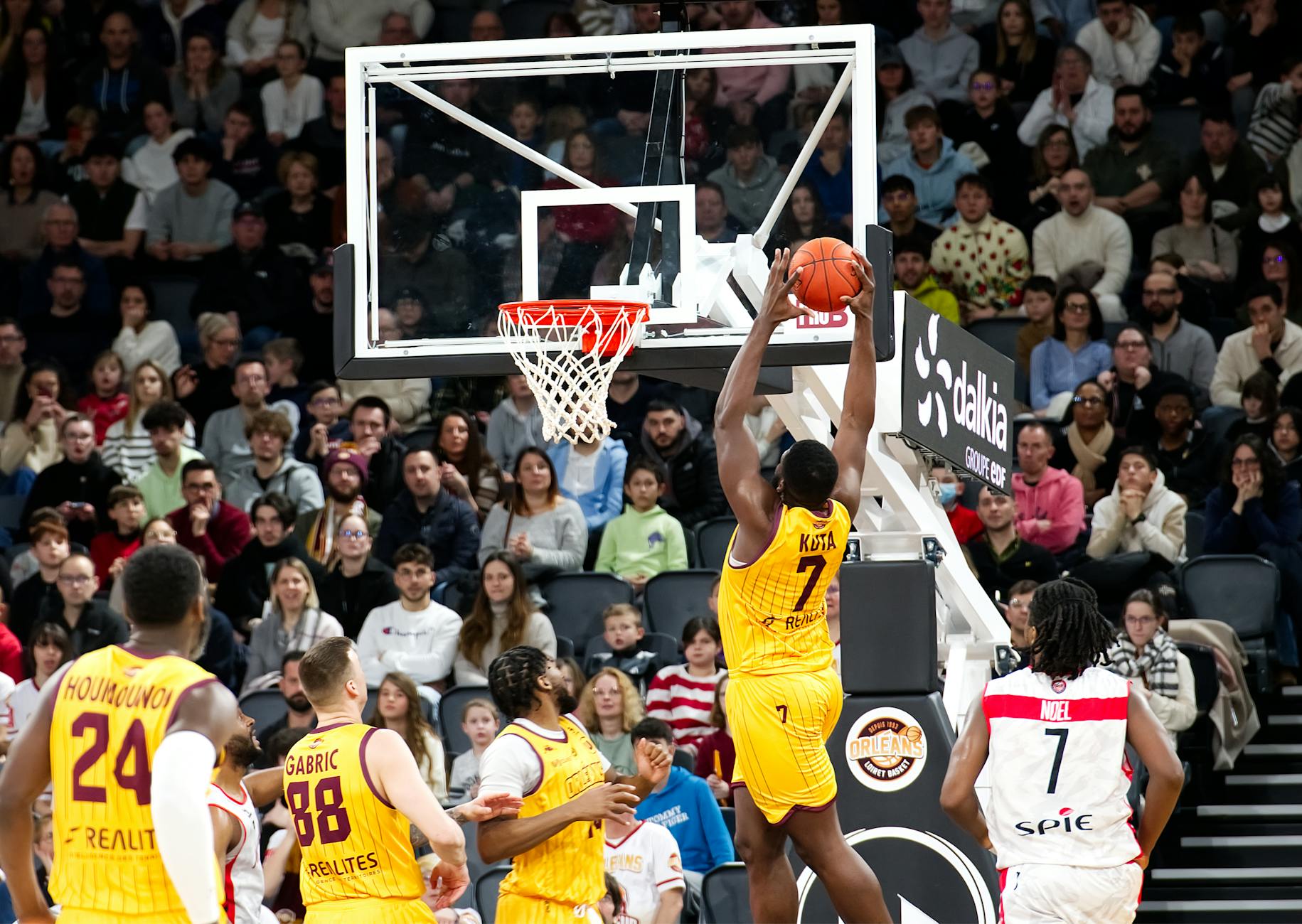 A player jumps to score during a thrilling basketball game with a full crowd.